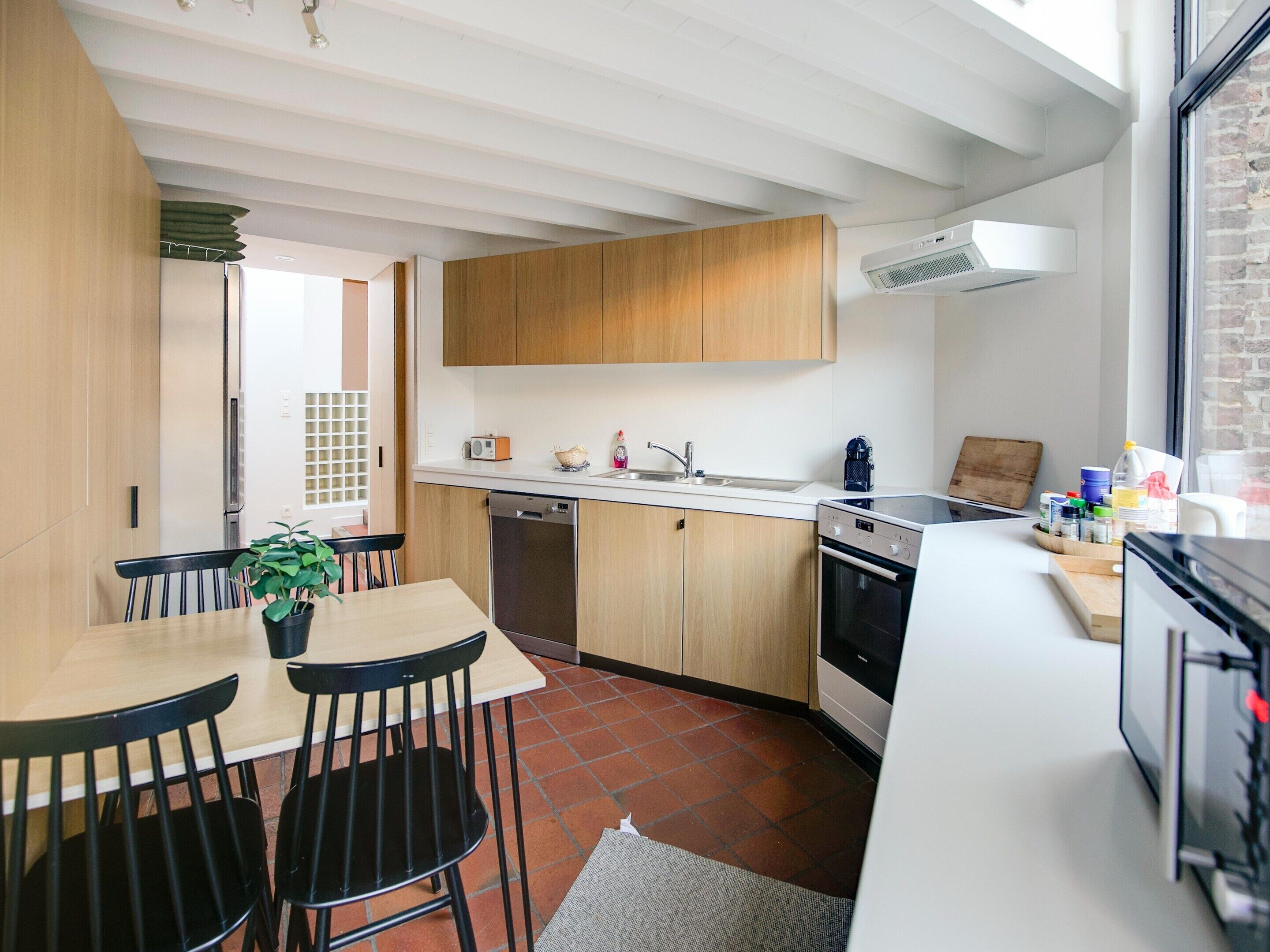 A modern kitchen with wooden cabinets, a white countertop, and a dining area with a table and chairs.