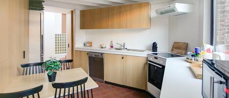 A modern kitchen with wooden cabinets, a white countertop, and a dining area with a table and chairs.