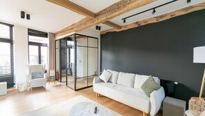 A modern living room with a white sofa, a round coffee table, and a large black accent wall. - Holiday Home in the Heart of Hasselt (Hasselt)