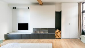 A modern living room with a flat-screen TV mounted on a white wall, a built-in fireplace, and a stack of firewood. - Holiday Home in the Heart of Hasselt (Hasselt)