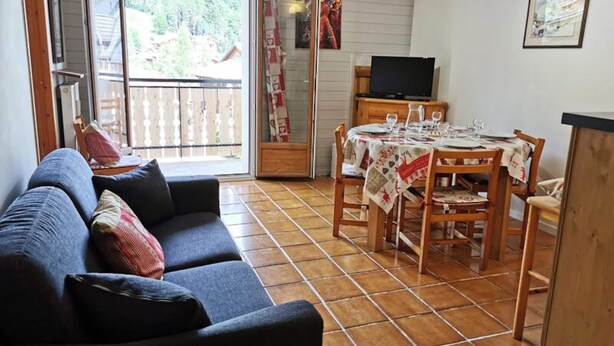 A living room with a sofa, a dining table set for four, and a television on a stand. - Apartment in Les Gets Near Mont Chery (Les Gets)