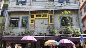 A multi-story building with balconies, a ground-level entrance with a purple awning, and a visible sign indicating 24-hour service. - Twin Comfort Stay Chic & Spacious Setup (Bangkok)
