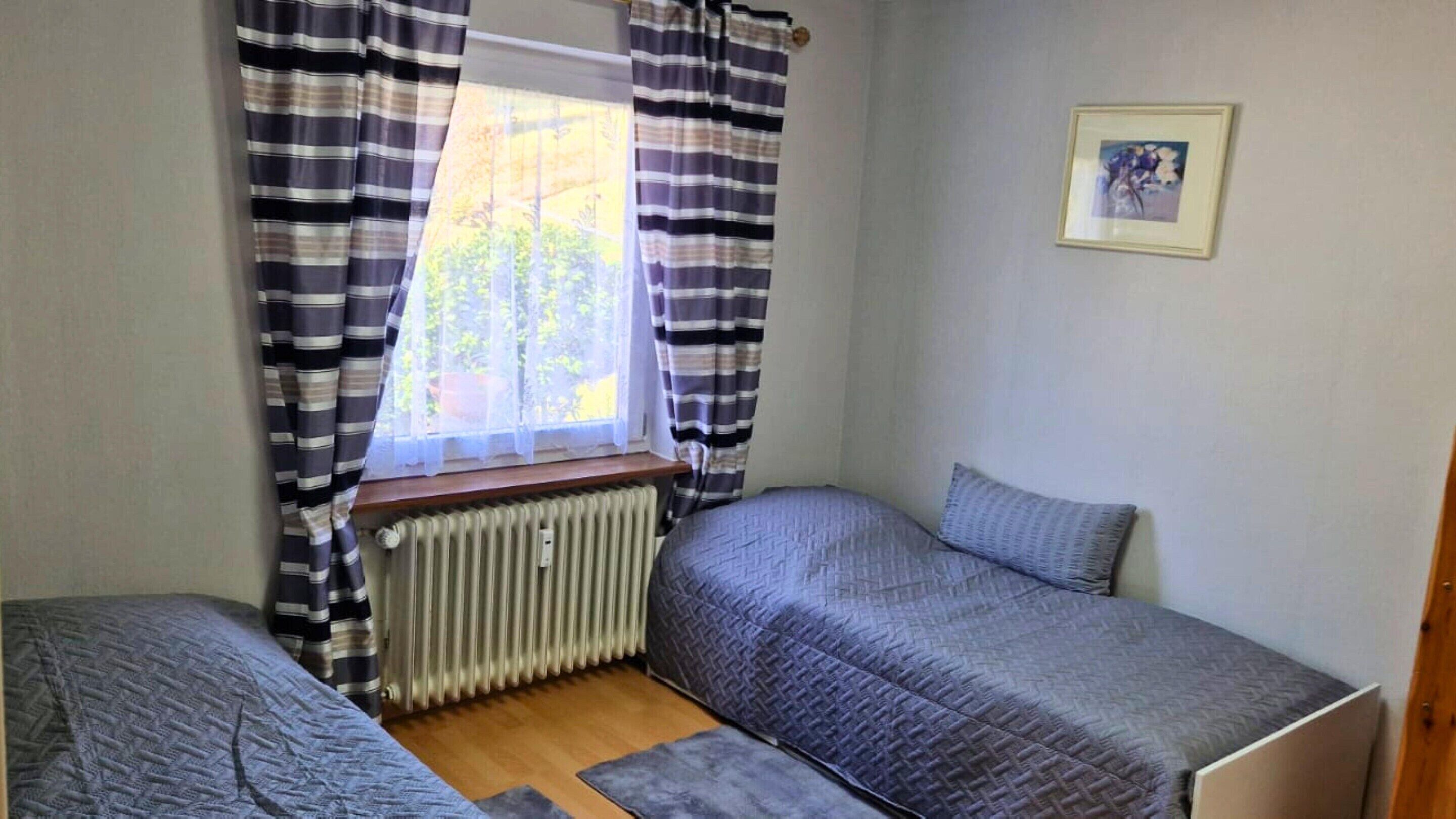 Un alojamiento pequeño y de una sola habitación con dos camas individuales, un radiador y una ventana con cortinas.
