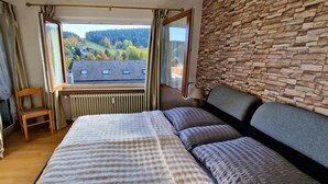 A bedroom with a large bed, a view of a house through a window, a radiator, and a stone wall. - House Sunshine on the ski Slope (Herrischried)