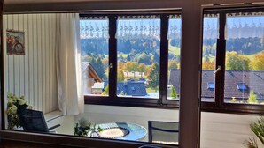 A room with a balcony, a dining table, and a view of a residential area with houses and trees. - House Sunshine on the ski Slope (Herrischried)