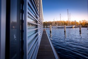 Una terraza de madera que se extiende sobre el agua, con vista a barcos y un edificio al fondo.