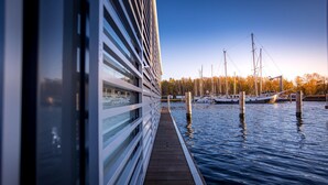 A wooden deck extending over water with a view of boats and a building in the background. - Floating Houseboat in Peenemunde (Peenemünde)