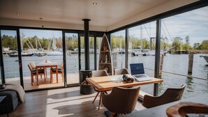 A modern interior with a wooden table, chairs, and a laptop. It features large windows offering a view of boats on water. - Floating Houseboat in Peenemunde (Peenemünde)
