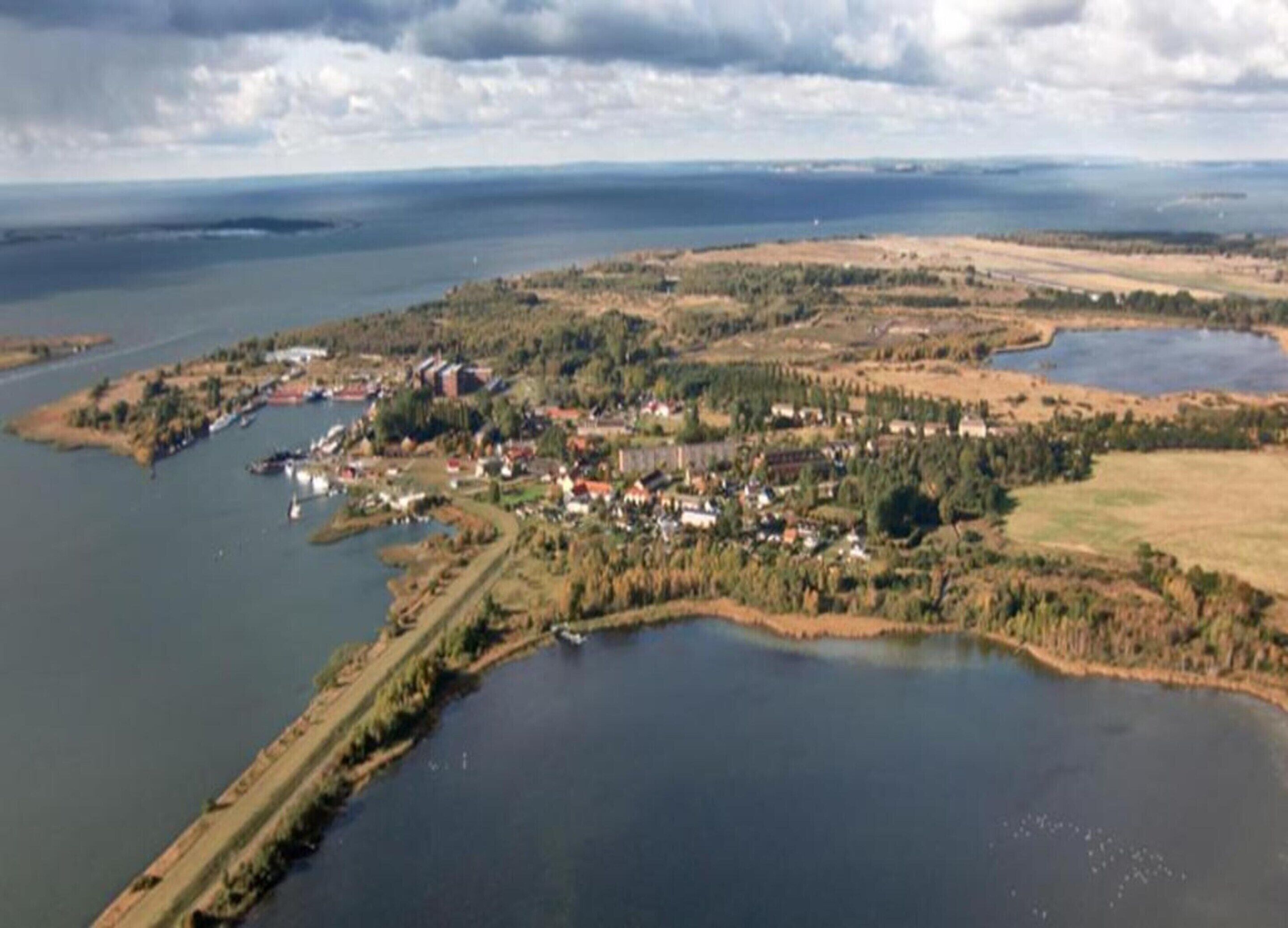 An aerial view of a coastal town with a marina, houses, and surrounding natural landscape.