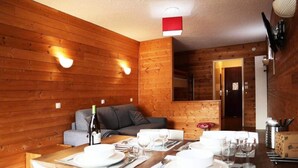 A wooden interior with a dining table set for four, a sofa, and a small kitchen area. - Apartment in Orres With Ski Access (Les Orres)