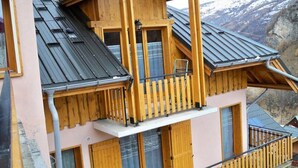 A wooden chalet with a balcony, large windows, and a view of a mountainous landscape. - 3-room Apartment for 6 People, 3-star Rating, South-facing (Valloire)