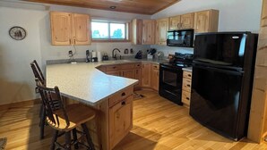 A kitchen with wooden cabinets, a black refrigerator, and a wooden dining table with chairs. - Mountain View Barndominium at Black Bear Ranch (Nordic)