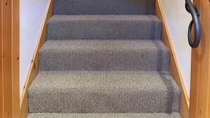 A wooden staircase with carpeted steps and a metal handrail, leading to a door marked with a 'B'. - Mountain View Barndominium at Black Bear Ranch (Nordic)