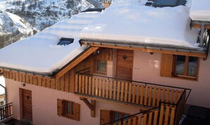 Een houten chalet met balkon en een met sneeuw bedekte dak, omgeven door bergen.
