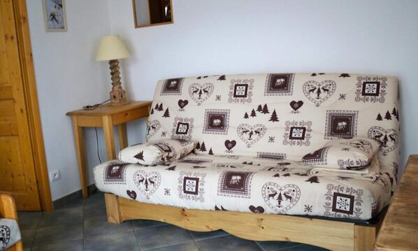 Een houten bank met een gestreept patroon, een klein houten bijzettafeltje met een lamp, en een ingelijst schilderij aan de muur.