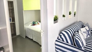 Ett sovrum med en säng, en vit dörr, en randig soffa och en liten hylla med växter.