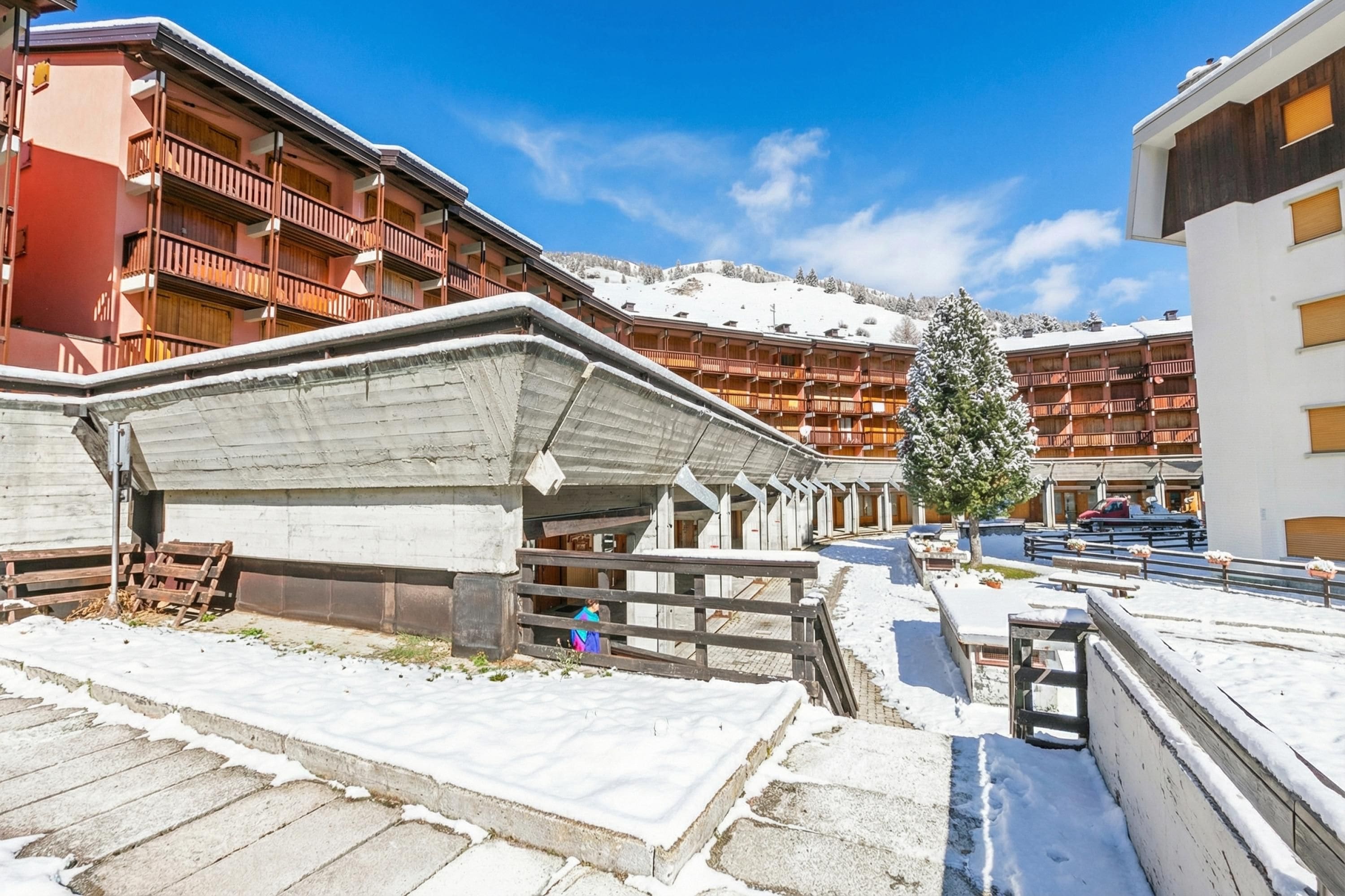 A hotel with multiple balconies, a snow-covered ground, and a view of a mountain.