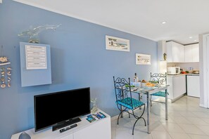 Un salon moderne doté d’un téléviseur à écran plat, d’une table à manger avec des chaises, d’un coin cuisine avec des placards et d’objets décoratifs sur les murs.