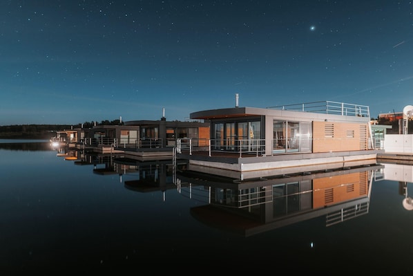 Une propriété située au bord de l’eau, dotée d’une architecture moderne, comprenant plusieurs bâtiments aux grandes fenêtres et offrant une vue sur une étendue d’eau scintillante.