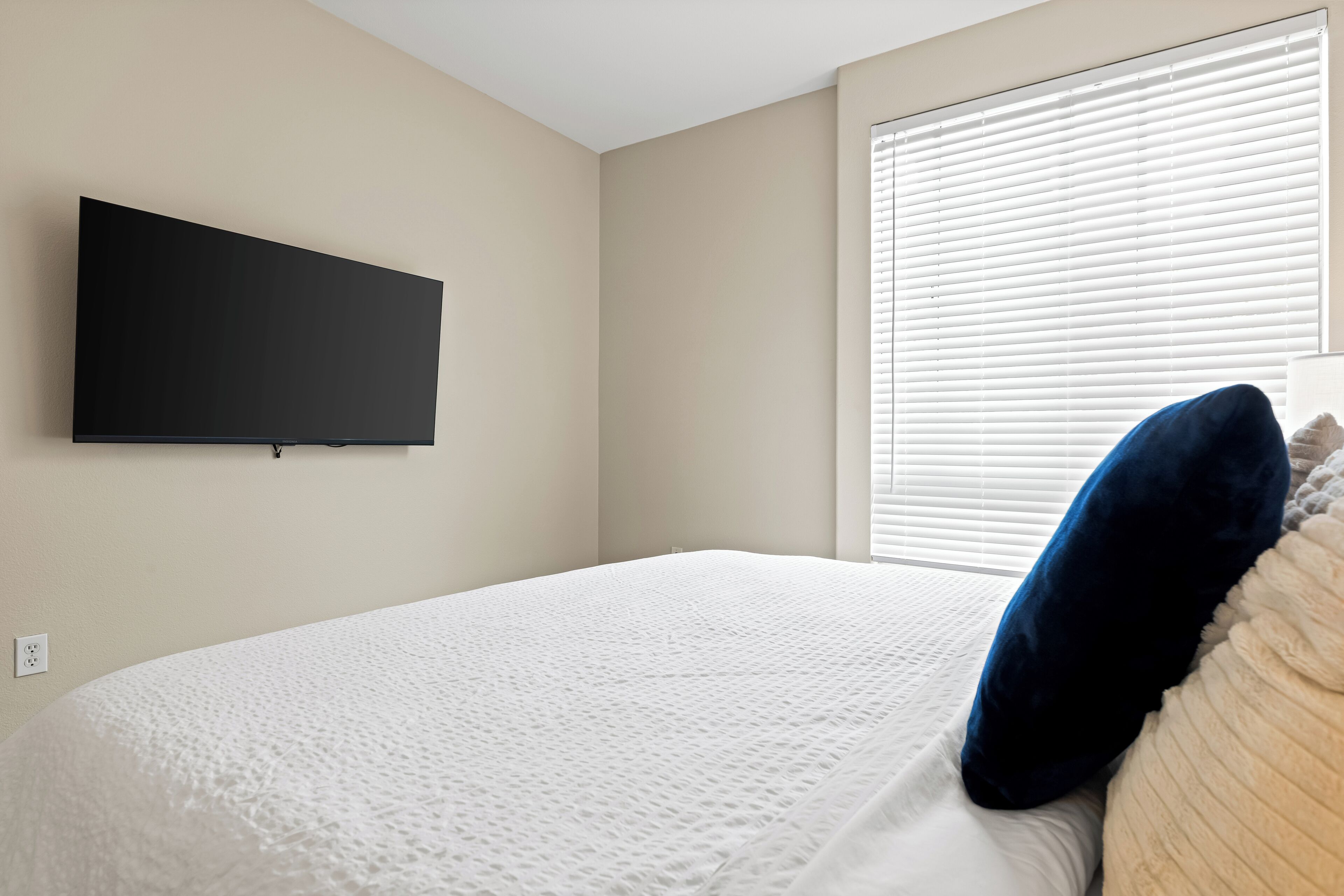 Een slaapkamer met een bed, een aan de muur bevestigde televisie en een raam met zonwering.