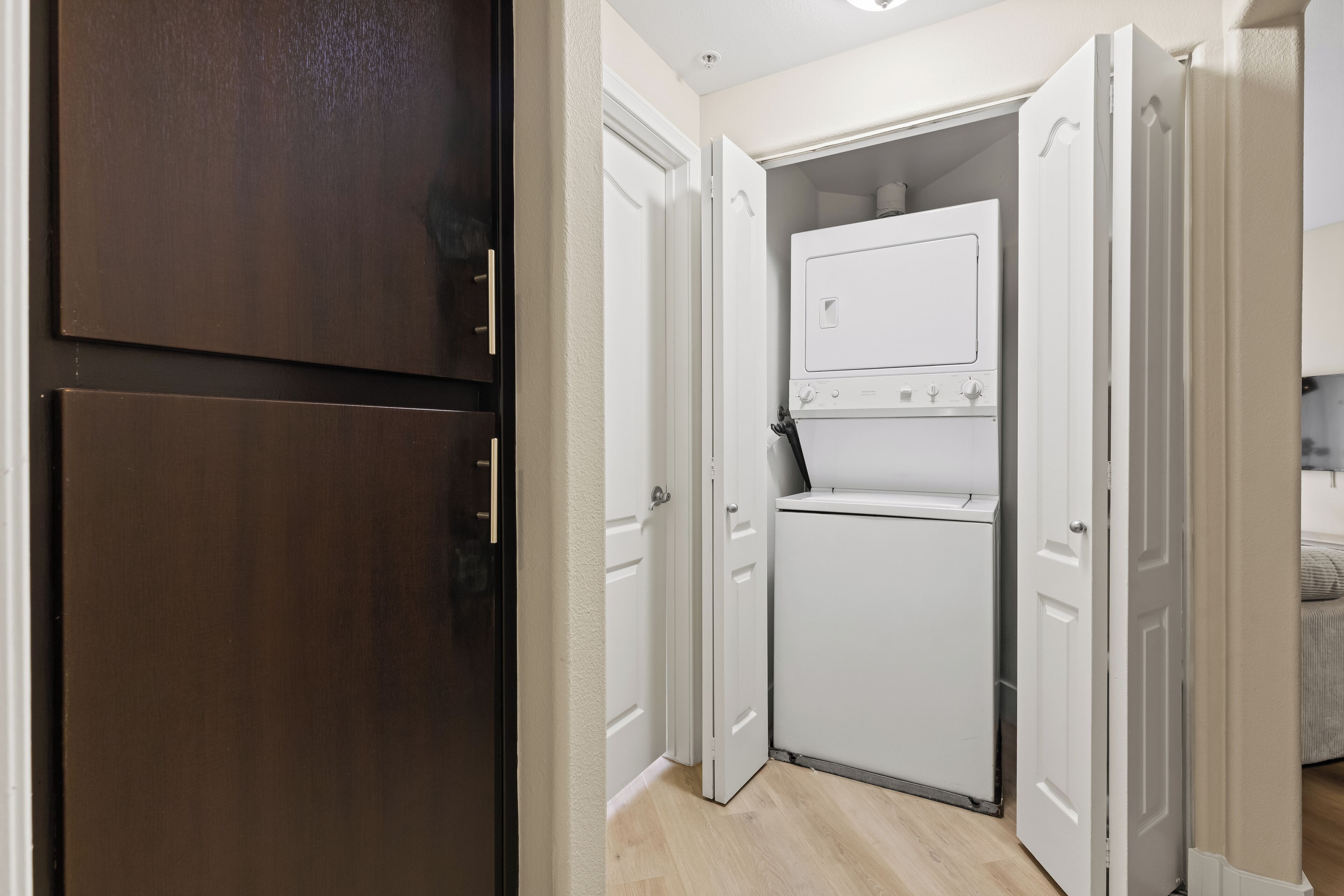 A compact laundry room with a white washer and dryer, wooden cabinets, and a door leading to another room.