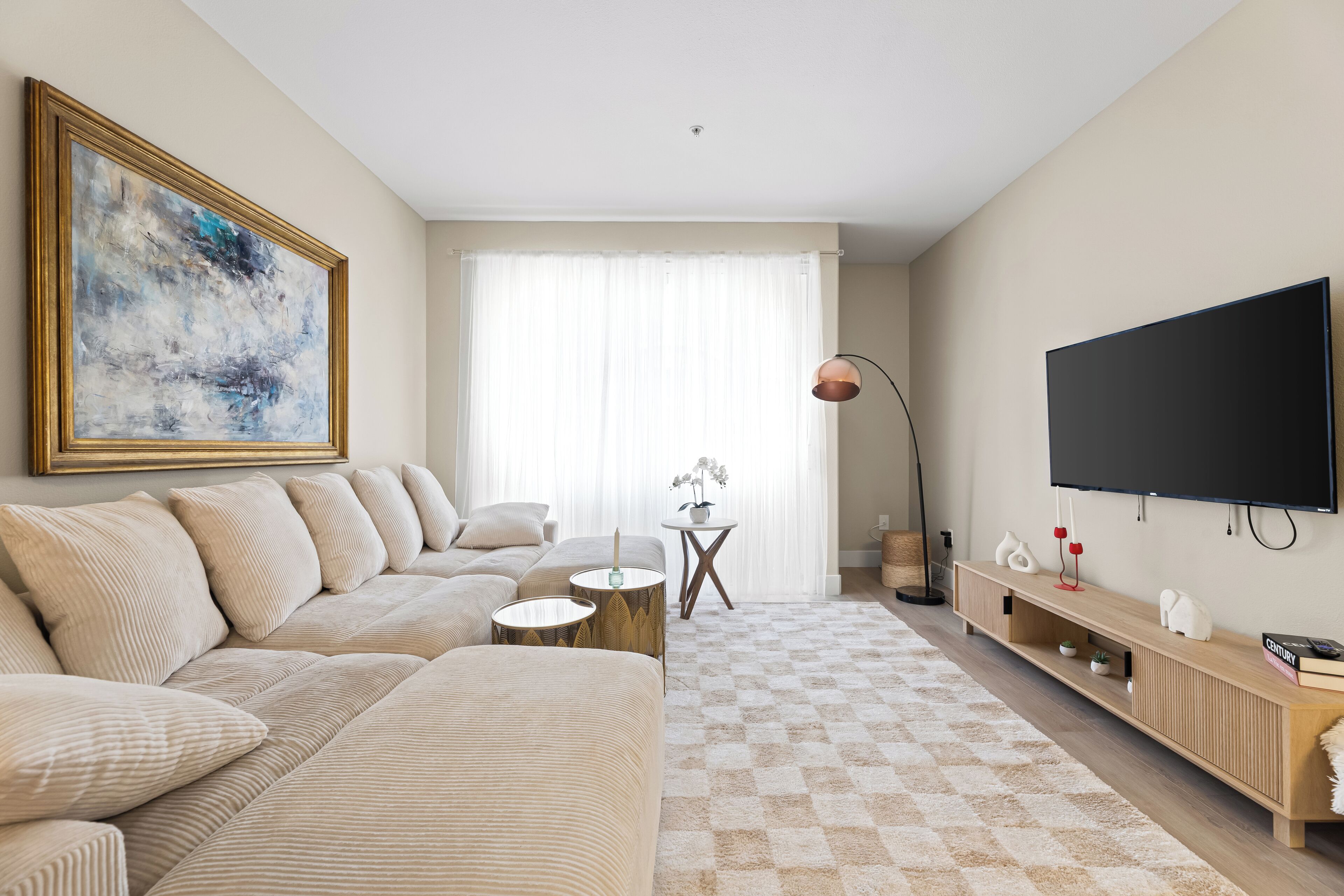 Ein modernes Wohnzimmer mit einem beigefarbenen Sofa, einem Flachbildfernseher und einem großen abstrakten Gemälde.