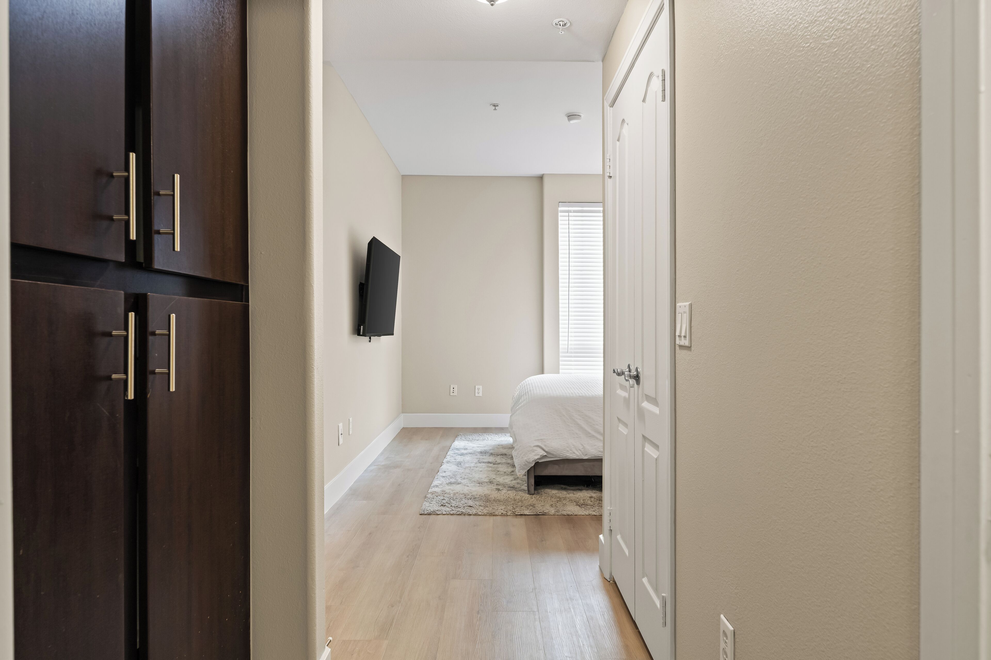 Un dormitori amb un llit, un televisor fixat a la paret, terres de fusta i una porta que dona a una altra habitació.