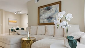 Ein modernes Wohnzimmer mit einem beigefarbenen Sofa, einem runden Couchtisch mit weißer Orchidee und einem goldenen Beistelltisch.