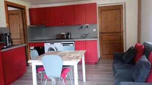 A compact kitchen with red cabinets, a washing machine, and a dining area with a table and chairs. - 2 Rooms 4 People 3 South Facing (Valloire)