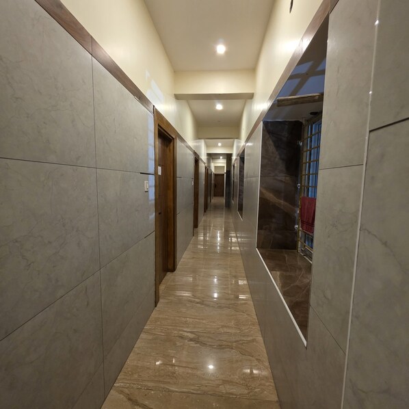 A hallway with marble flooring and walls, wooden doors, and a ceiling with recessed lighting. - Hotel Raja Grand (Tiruvannamalai)