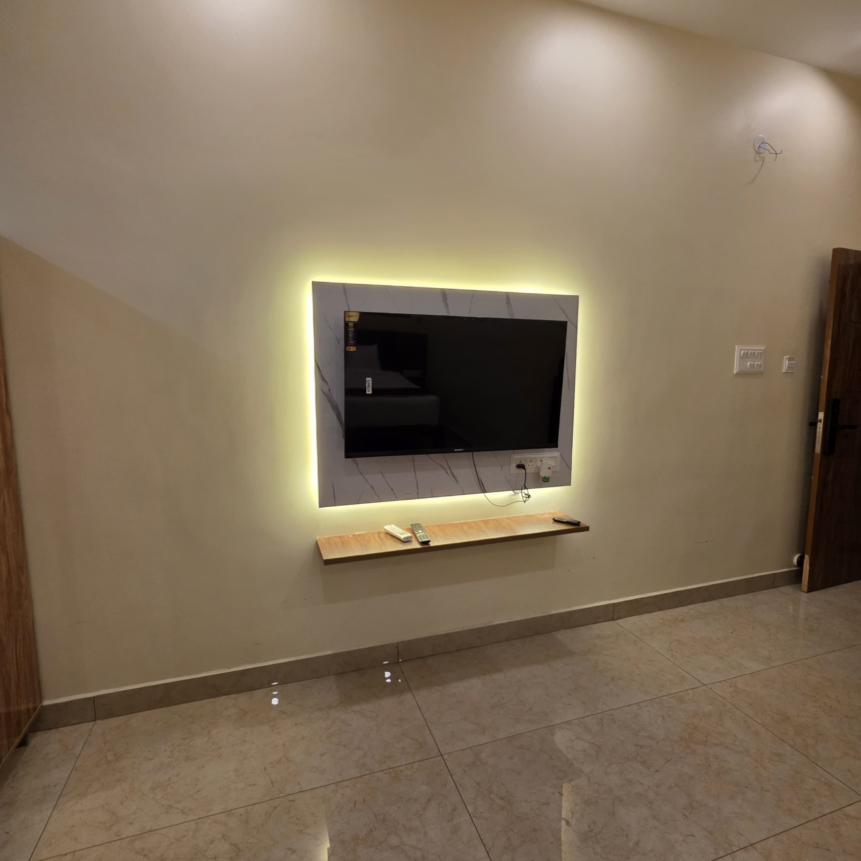 Una sala de estar moderna con un televisor de pantalla plana montado en la pared, un estante de madera debajo y piso de baldosas.
