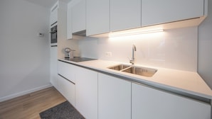 Et moderne køkken med hvide skabe, en stålvask og en indbygget ovn.