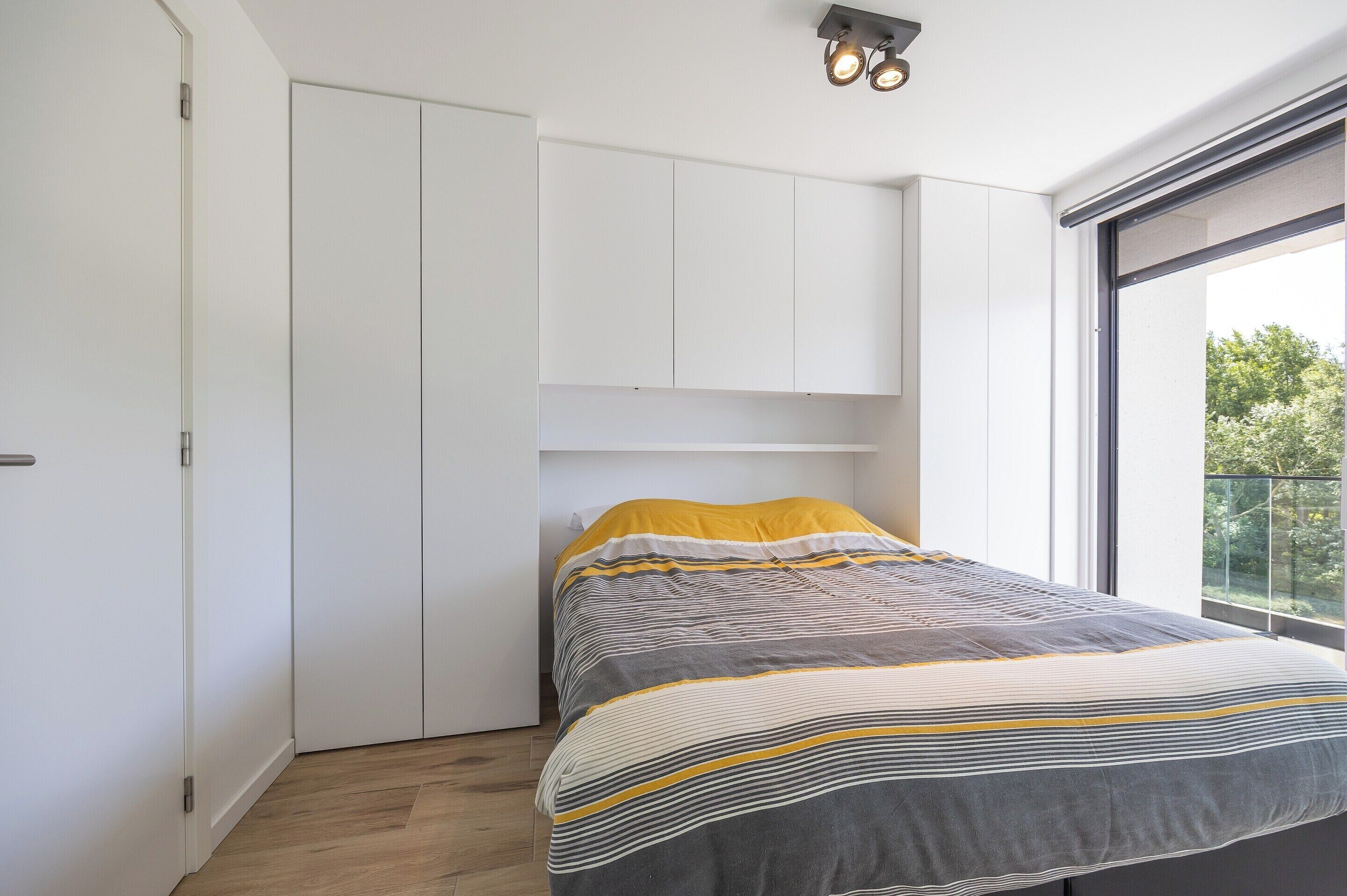 Een slaapkamer met een bed, een witte kledingkast en een raam met uitzicht.