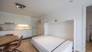 Et lille værelse med seng, spisebord med stole og tekøkken.