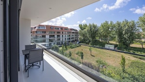 En balkon med gelænder af glas, udsigt over en græsplæne og en bygning med mange vinduer.