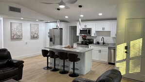 Uma cozinha moderna com armários brancos, uma ilha central com banquetas, um ventilador de teto e iluminação embutida.