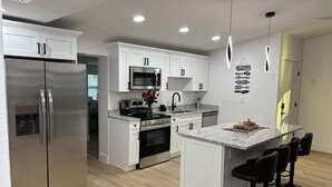 Cozinha moderna com armários brancos, eletrodomésticos de aço inoxidável, uma ilha central com banquetas e iluminação pendente.