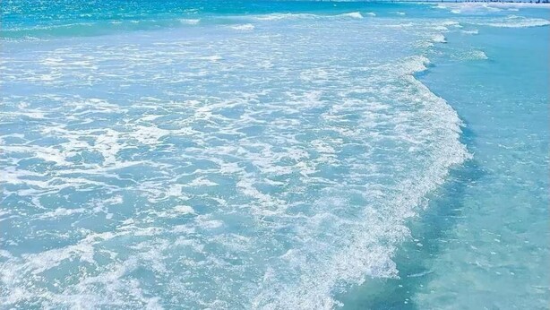 Uma praia com águas azul-claras e areal arenoso.