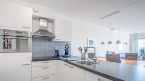 A modern kitchen with white cabinets, a stainless steel range hood, a built-in oven, a coffee maker, and a sink. - 4-person Apartment With Island-sea View (De Koog)