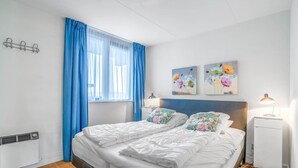 A bedroom with a bed, a bedside table, a lamp, and a wall-mounted heater. - 4-person Apartment With Island-sea View (De Koog)