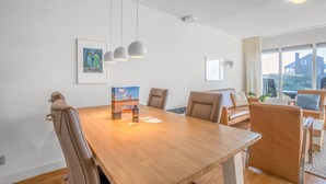 A modern dining area with a wooden table, leather chairs, pendant lights, and a view of the outside through large windows. - 4-person Apartment With Island-sea View (De Koog)