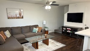 A living room with a sofa, coffee table, TV, and a ceiling fan.