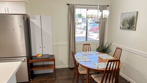 A compact kitchen with a refrigerator, a dining table with chairs, and a window with curtains.