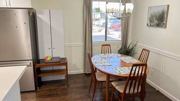 Una cocina compacta con refrigerador, una mesa de comedor con sillas y un ventanal con cortinas.