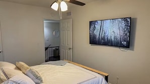 A bedroom with a bed, a ceiling fan, a TV on the wall, and a door leading to a staircase.