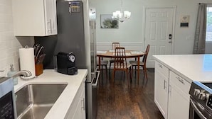 A modern kitchen with white cabinetry, a stainless steel sink, a black refrigerator, and a dining area with a wooden table and chairs.