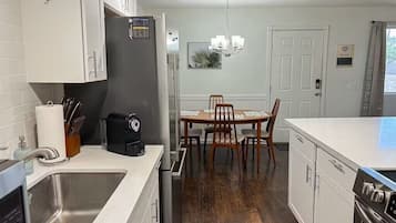 A modern kitchen with white cabinetry, a stainless steel sink, a black refrigerator, and a dining area with a wooden table and chairs.