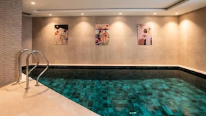 A swimming pool with clear water, a metal ladder, and three artworks on the wall. - Apartment in Meribel With Pool & Jacuzzi (Les Allues)