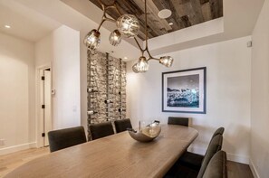Ein Essbereich mit einem Holztisch, sechs Stühlen, einer Chandelierleuchtre, einem Weinkühlschrank und einem gerahmten Bild an der Wand.