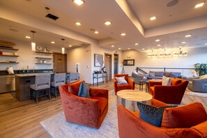 Ein modernes Wohnzimmer mit Küchenbereich, das eine Bar, Sitzgelegenheiten mit orangefarbenen Sofas und einen Essbereich bietet.